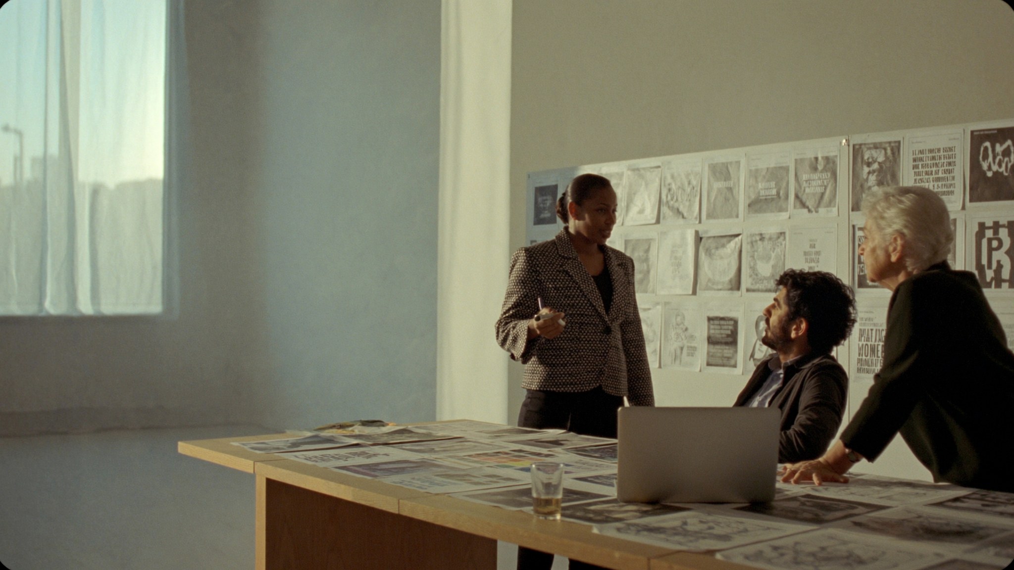 A marketing team working through printed campaign layouts on a long table in late-afternoon light